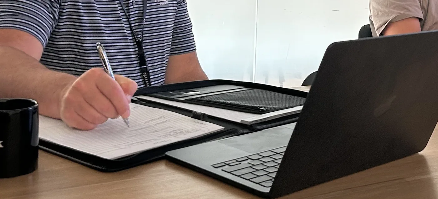 A colleague taking handwritten notes beside a laptop during a working session